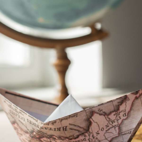 A photograph of a globe and a boat made of paper from a map, both resting on a table.